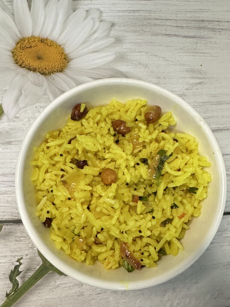 A bowl of Chitranna, a South Indian rice dish, garnished with fresh coriander leaves. The rice is mixed with mustard seeds, curry leaves, green chilies, and peanuts and lemon.