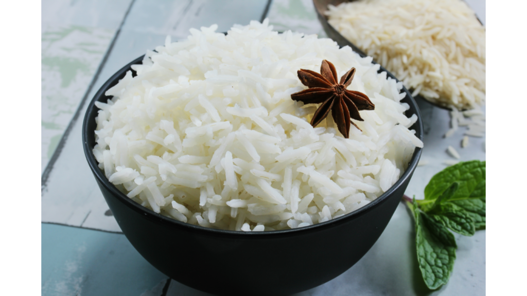 A close-up photo of fluffy, cooked rice grains in a white bowl on a wooden table.